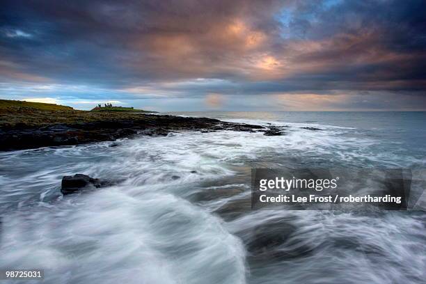 view along coastline on a stormy day towards the ruins of dunstanburgh castle, northumberland, england, united kingdom - craster stock-fotos und bilder