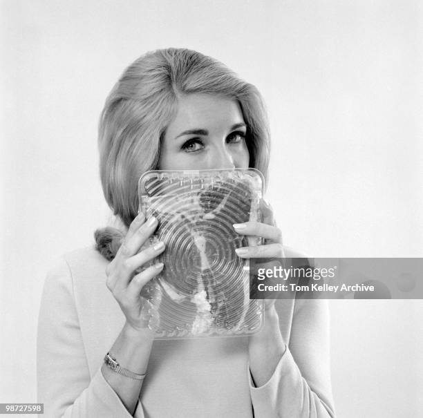 An unidentified model holds a packaged cut of meat in front of her face and looks over the top of it, 1967.