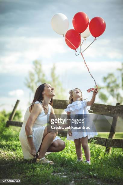 giovane donna con bambino in abito bianco con palloncini colorati all'aperto - mamma bambina palloncino bianco foto e immagini stock
