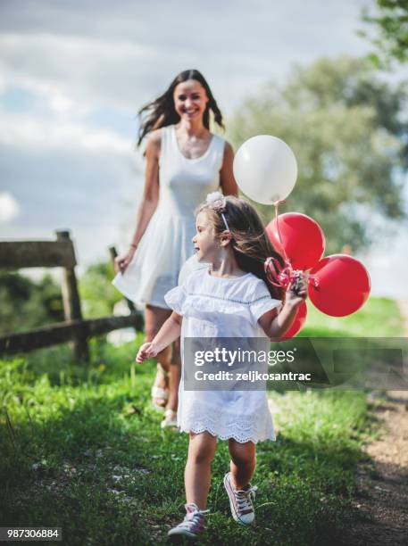 giovane donna con bambino in abito bianco con palloncini colorati all'aperto - mamma bambina palloncino bianco foto e immagini stock