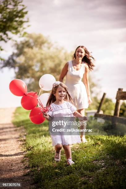 giovane donna con bambino in abito bianco con palloncini colorati all'aperto - mamma bambina palloncino bianco foto e immagini stock