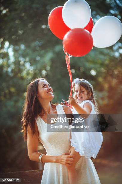 giovane donna con bambino in abito bianco con palloncini colorati all'aperto - mamma bambina palloncino bianco foto e immagini stock