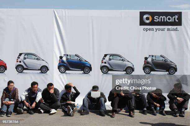 Chinese visitors rest in front of an advertisement billboard at the Beijing Auto Show on April 29, 2010 in Beijing, China. The Beijing auto show has...