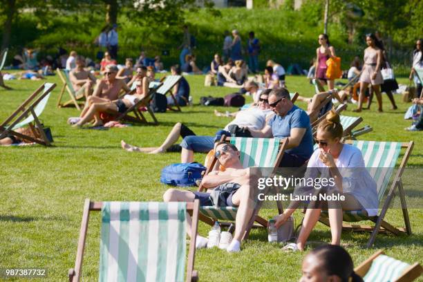 people sat on deck chairs relaxing in the sun shine, green park, london, england - sun deck stock-fotos und bilder