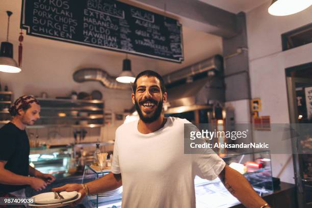 smiling waiter in a busy fast food restaurant - crowded restaurant stock pictures, royalty-free photos & images