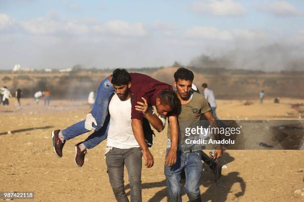 Palestinian protestors carry a injured protestor after Israeli forces intervene them on the 14th week of right of return march along the border with...