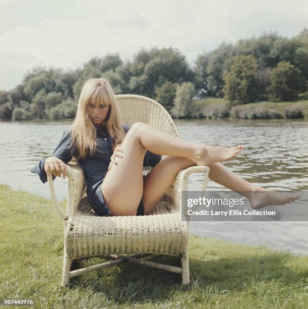 English actress Susan George posed wearing a blue blouse, seated on a wicker chair beside a river in England in 1972.