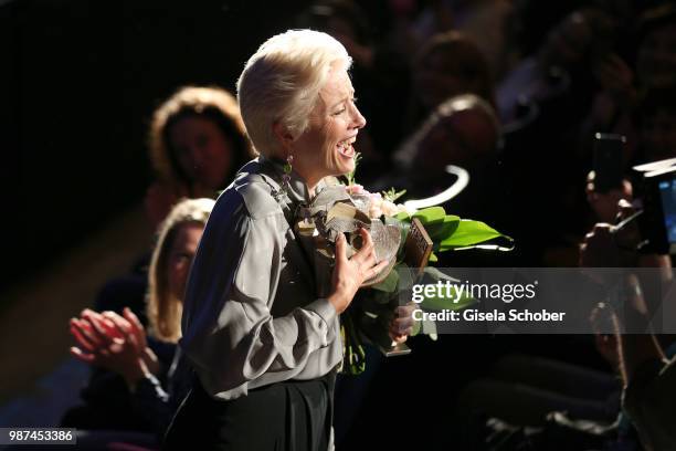 Emma Thompson barefoot on stage with her shoes in her mouth and the award at the Cine Merit Award Gala during the Munich Film Festival 2018 at...