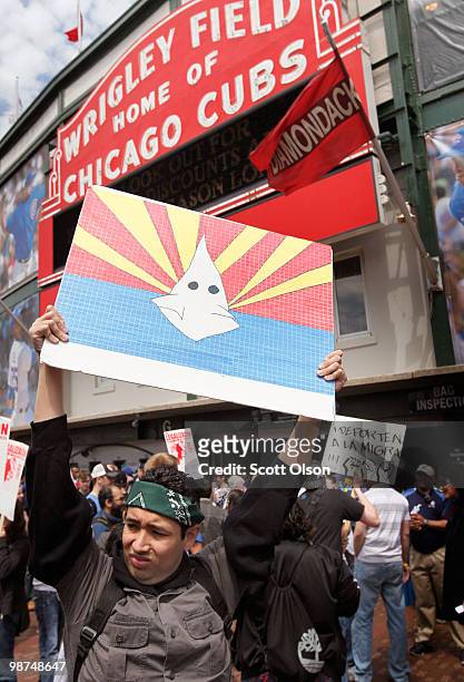 Jose Munoz holds a poster of the Arizona Flag with a Ku Klux Klansman in the center during a protest outside Wrigley Field before the start of the...