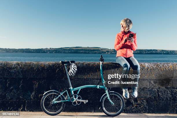 senior woman with bike and phone. - cycling scotland stock pictures, royalty-free photos & images