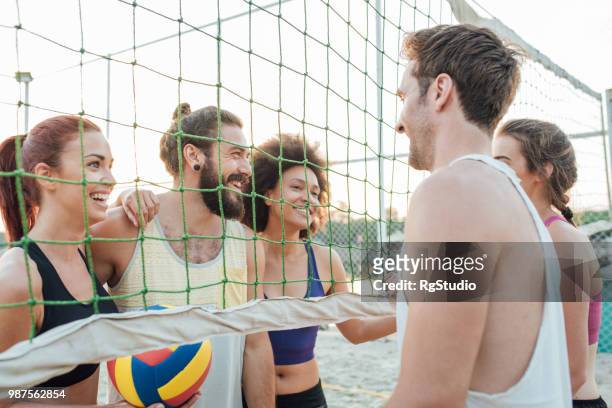 atletas felices reunidos en torno a la red del voleibol en la playa - campeón de torneo fotografías e imágenes de stock
