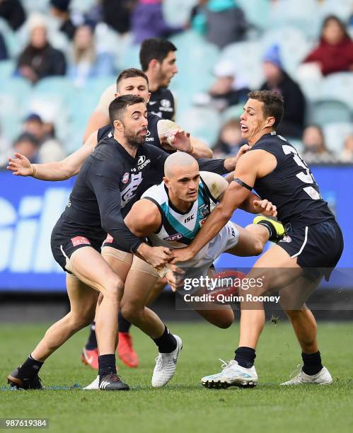 Sam Powell-Pepper of the Power handballs whilst being tackled by Kade Simpson and Ed Curnow of the Blues during the round 15 AFL match between the...