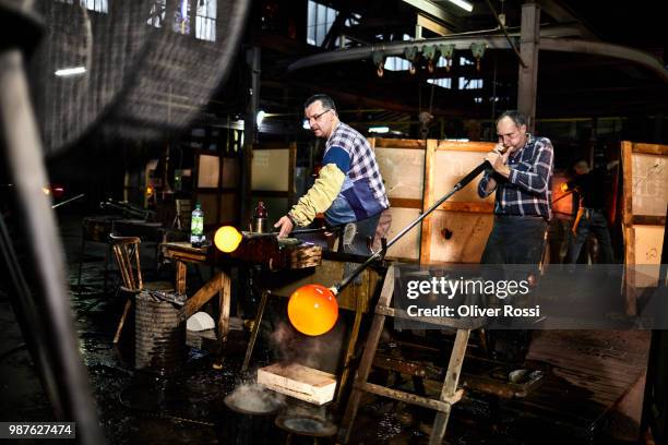 two glass blowers working with blowpipes on glowing glass in glass factory - blowgun stock pictures, royalty-free photos & images