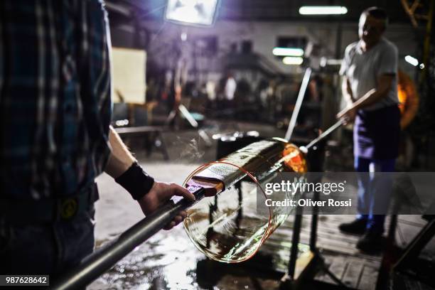 two glass blowers working on glass in a factory - glass factory stock-fotos und bilder