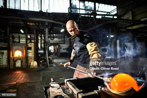 glass blower working with blowpipe on glowing glass in glass factory - stahlindustrie stock-fotos und bilder