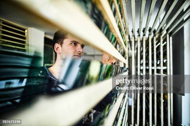 young man examining assortment of stained glass on a rack - glass factory stock-fotos und bilder