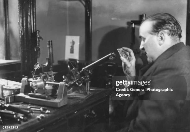 Gunsmith and ballistics expert Robert Churchill using a microscope to help compile a ballistic report for Scotland Yard in the case of the murder of...