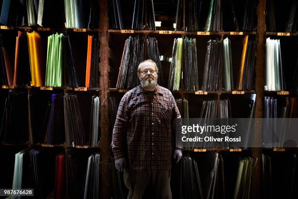 portrait of senior man standing at shelf with assortment of stained glass - glass factory stock-fotos und bilder