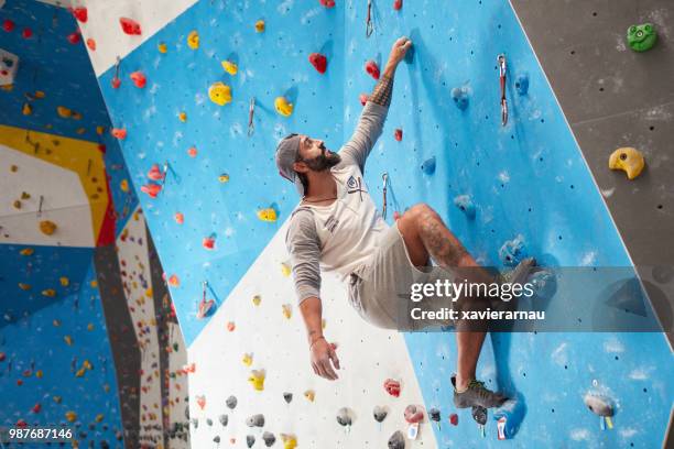 sportieve volwassen man klimmuur in sportschool - boulderen stockfoto's en -beelden