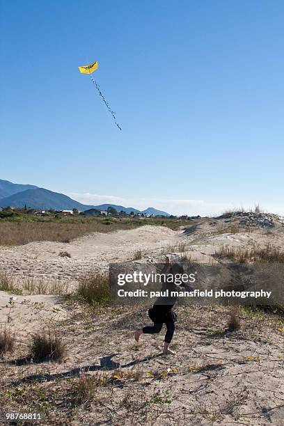 girl running with kite on sand dunes - paul mansfield photography stock-fotos und bilder