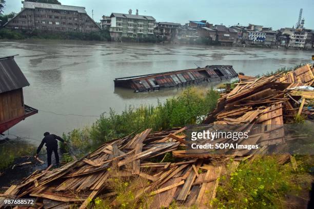 Man collects the wooden sheets from a damaged houseboat. A flood alert has been sounded in Kashmir in the wake of continuous rains since Wednesday....