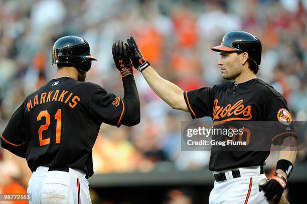 Nick Markakis of the Baltimore Orioles is congratulated by Luke Scott after scoring in the first inning against the Boston Red Sox at Camden Yards on...