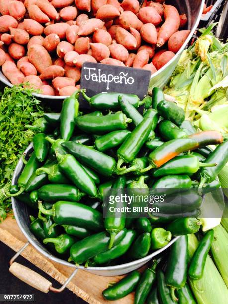 green jalapeno peppers in a bucket at a farmer's market-baby yams in the background - jalapeno stock pictures, royalty-free photos & images