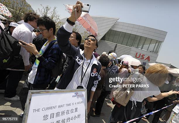 Visitors wait in line in front of a sign saying "The current wait time is 4 hours" at the USA pavillion on the first day of the World Expo in...