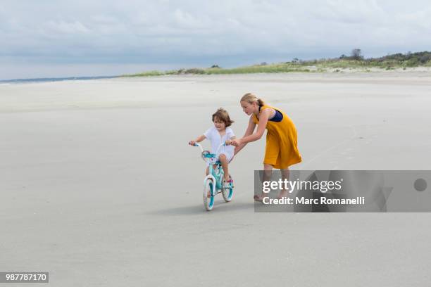 sister teaching her brother to bike - marc romanelli stock pictures, royalty-free photos & images