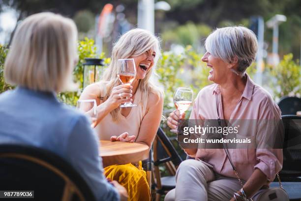 happy senior women drinking wine and laughing together at restaurant - drink stock pictures, royalty-free photos & images