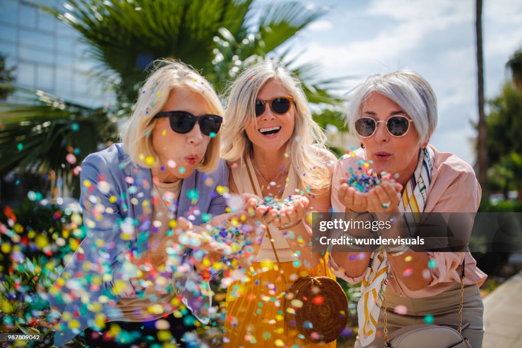 Cheerful senior women celebrating by blowing confetti in the city