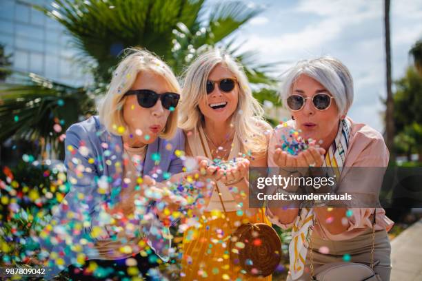 alegres mulheres sênior celebrando soprando confete na cidade - female friendship - fotografias e filmes do acervo
