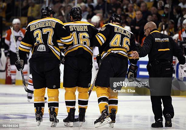 Patrice Bergeron and David Krejci of the Boston Bruins help teammate Marco Sturm off the ice in the first period against the Philadelphia Flyers in...