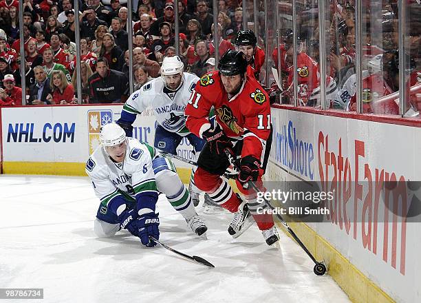 John Madden of the Chicago Blackhawks grabs the puck from the boards as Christian Ehrhoff of the Vancouver Canucks reaches around and Pavol Demitra...