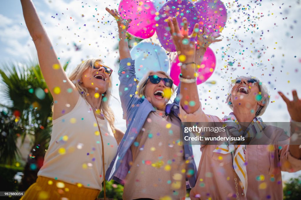 Excited mature women celebrating with colorful confetti and balloons outdoors