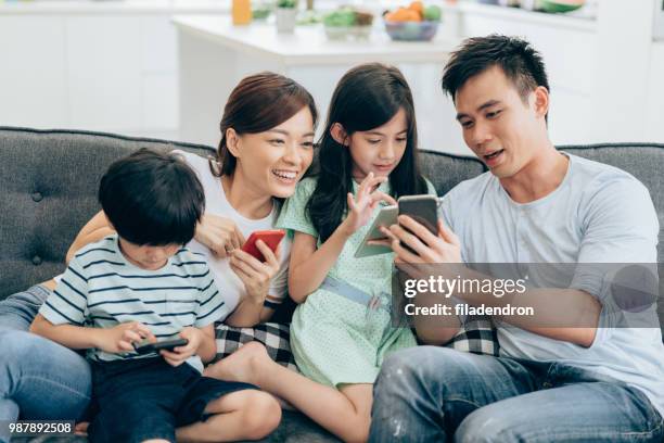 ontspannen thuis met draadloze technologie - asian young family stockfoto's en -beelden