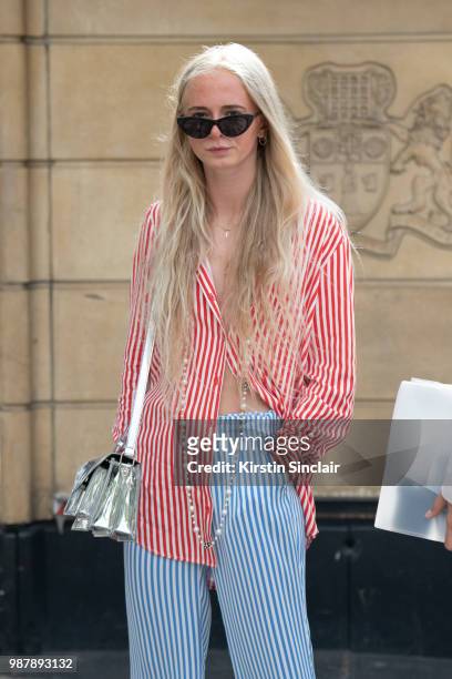 Guest wears a striped shirt and trousers with a silver bag during London Fashion Week Men's on June 10, 2018 in London, England.
