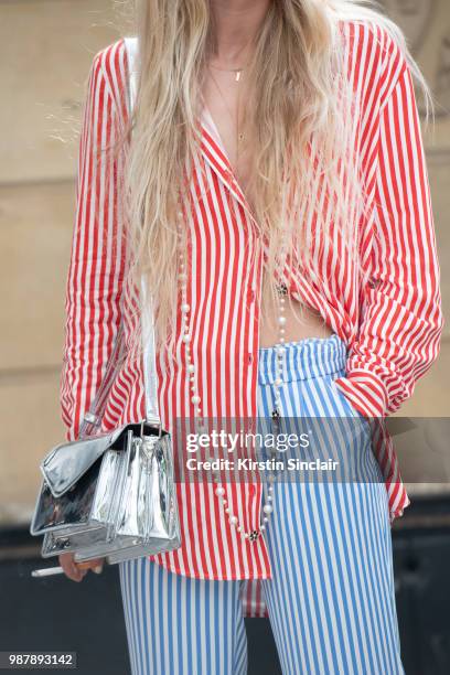 Guest wears a striped shirt and trousers with a silver bag during London Fashion Week Men's on June 10, 2018 in London, England.