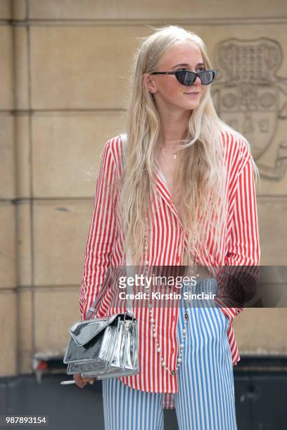 Guest wears a striped shirt and trousers with a silver bag during London Fashion Week Men's on June 10, 2018 in London, England.