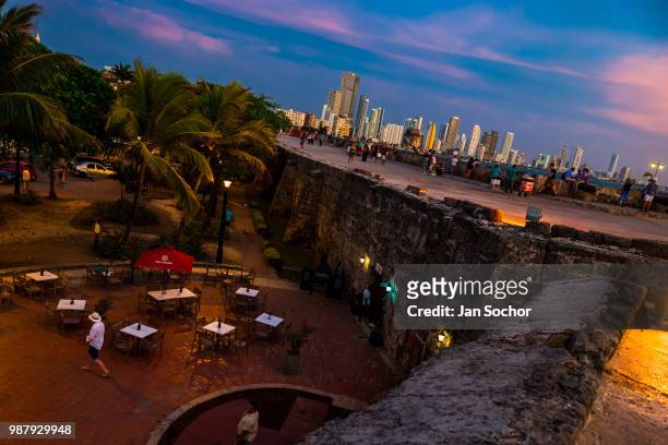 Tourists walk on and along the stone walls, surrounding the colonial walled city, at twilight on April 14, 2018 in Cartagena, Colombia. After the...