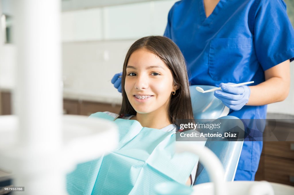 Dentist Standing Behind Smiling Teenage Girl With Braces In Clinic
