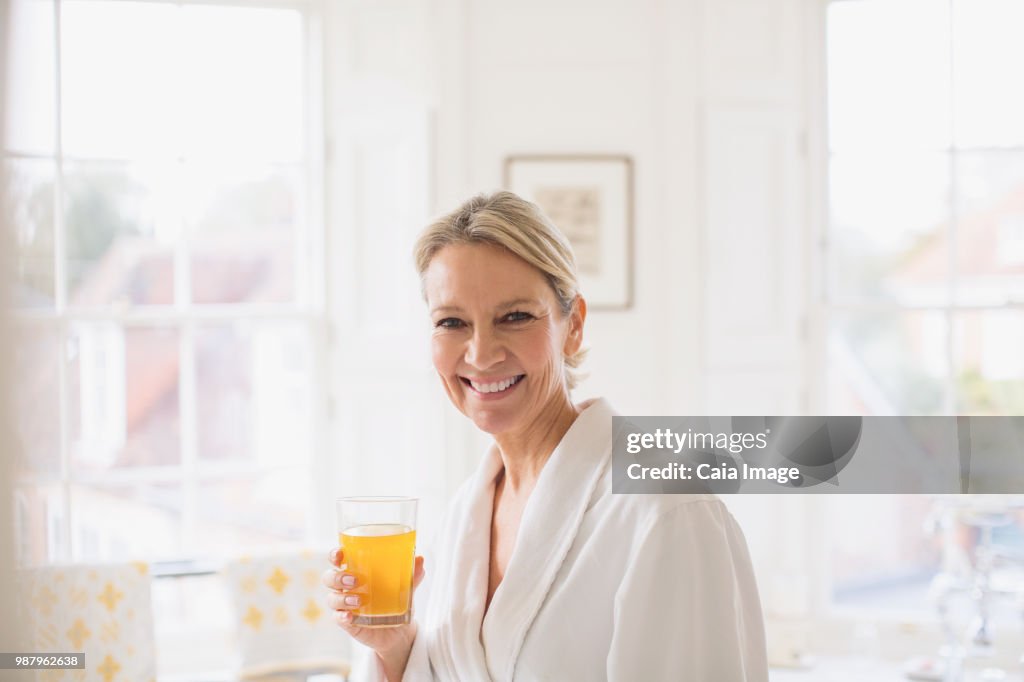 Portrait smiling, confident mature woman in bathrobe drinking juice