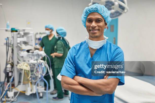 male nurse standing arms crossed in operating room - operating gown stock pictures, royalty-free photos & images