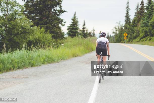 female cyclist rides along a rural highway - south central alaska stock pictures, royalty-free photos & images