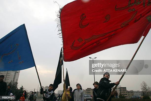 Young Iranian boys wave flags with the Arabic writing "Oh, Hussein" during a religious mourning event to mark Ashura in Tehran on December 26, 2009....