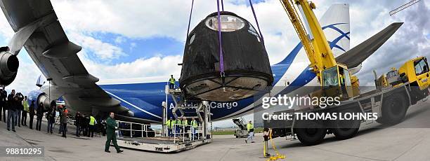 The reentry module of the Soyuz TM-19 mission is being loaded from an Airbus plane on a flat bed trailer after arriving at the airport in...
