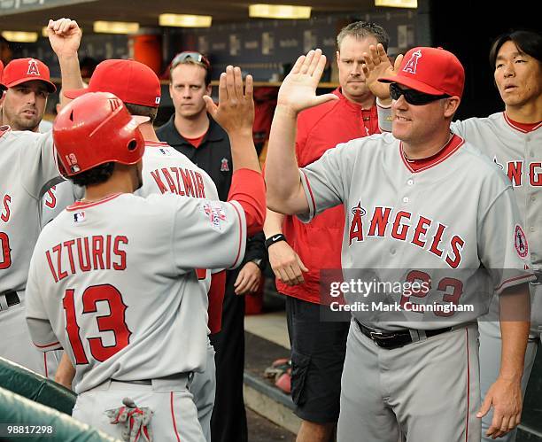 Maicer Izturis and coach Mike Butcher of the Los Angeles Angels of Anaheim high-five in the dugout against the Detroit Tigers during the game at...