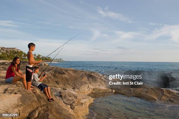 mixed race children fishing in ocean - inti st clair stock pictures, royalty-free photos & images