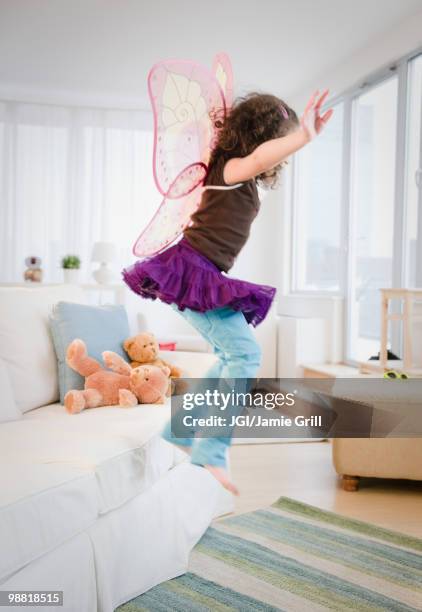 hispanic girl in fairy wings jumping off couch - imitazione-di-animali foto e immagini stock