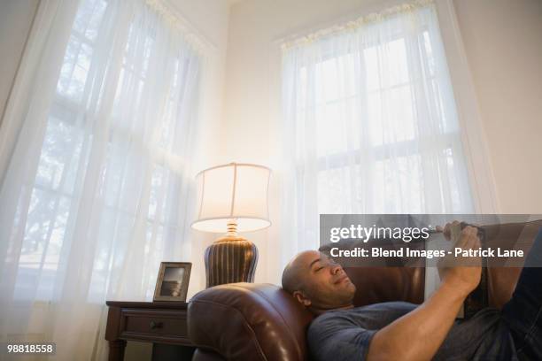 mixed race man laying on sofa reading book - arts express yourself 2009 stock pictures, royalty-free photos & images